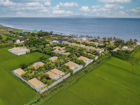An aerial view of a coastal residential area with houses, green fields, and a beach. - The Royal Purnama Luxury Villas - Adults Only (Sukawati)