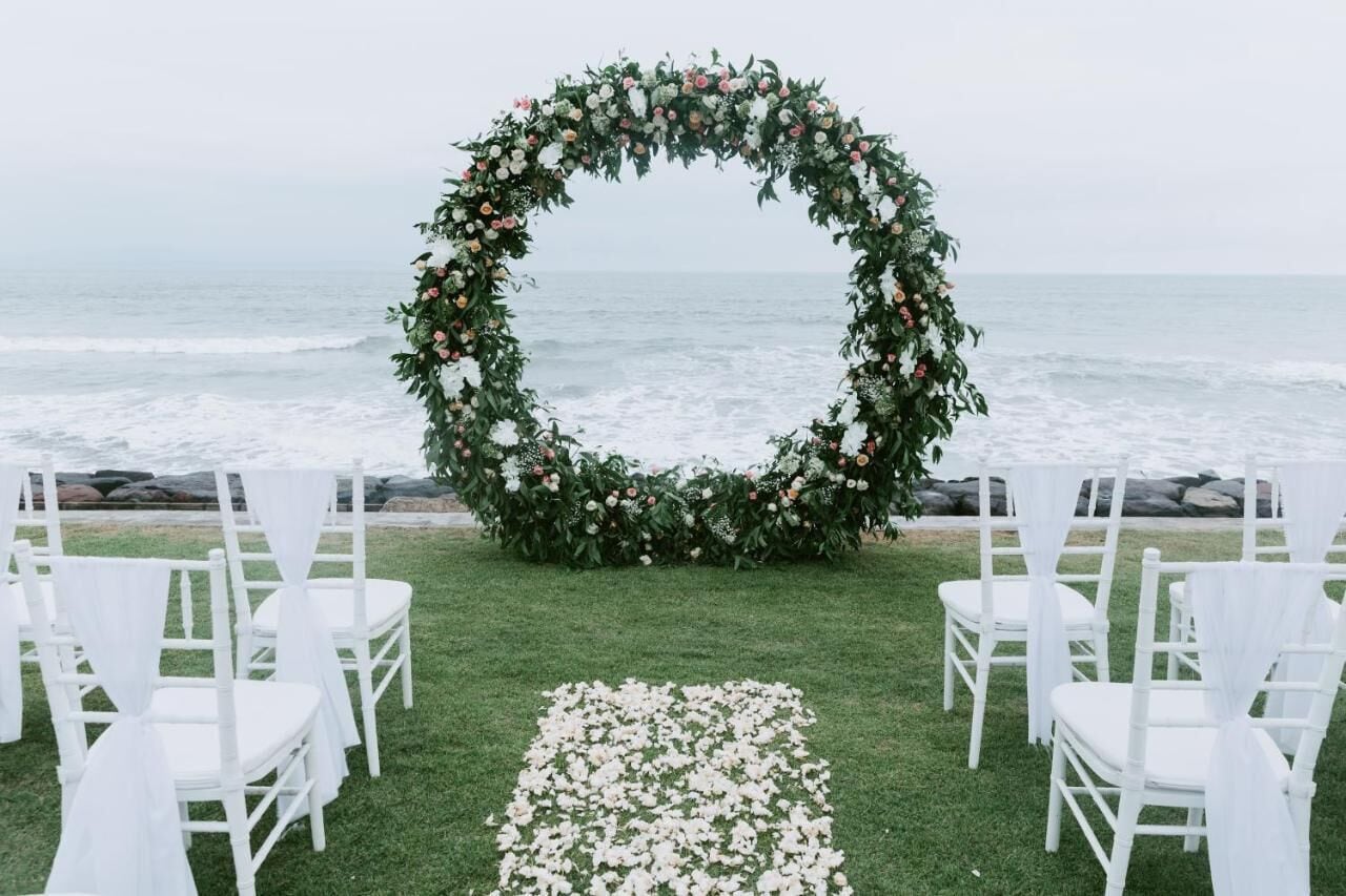 Decoración para boda al aire libre con un arco floral y sillas blancas dispuestas en un césped.