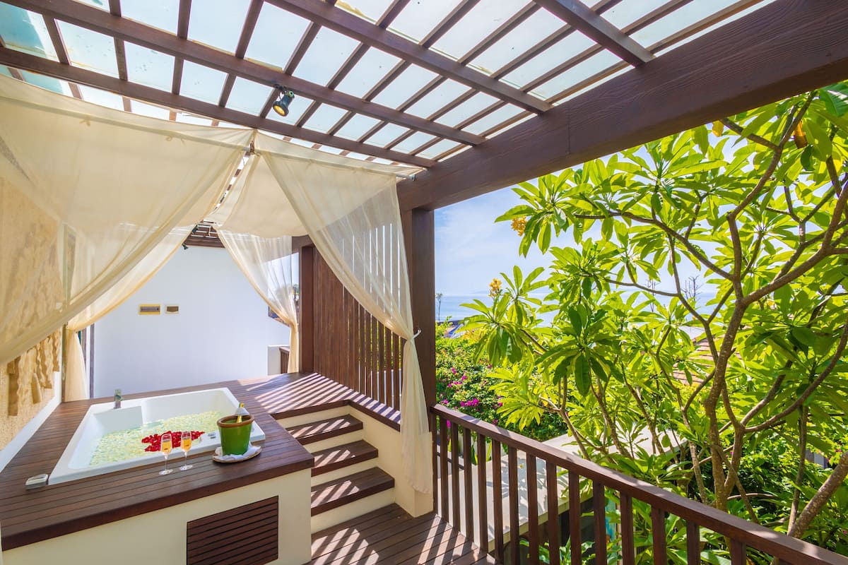 A balcony with a wooden floor, a white bathtub, and a glass door leading to a white room.