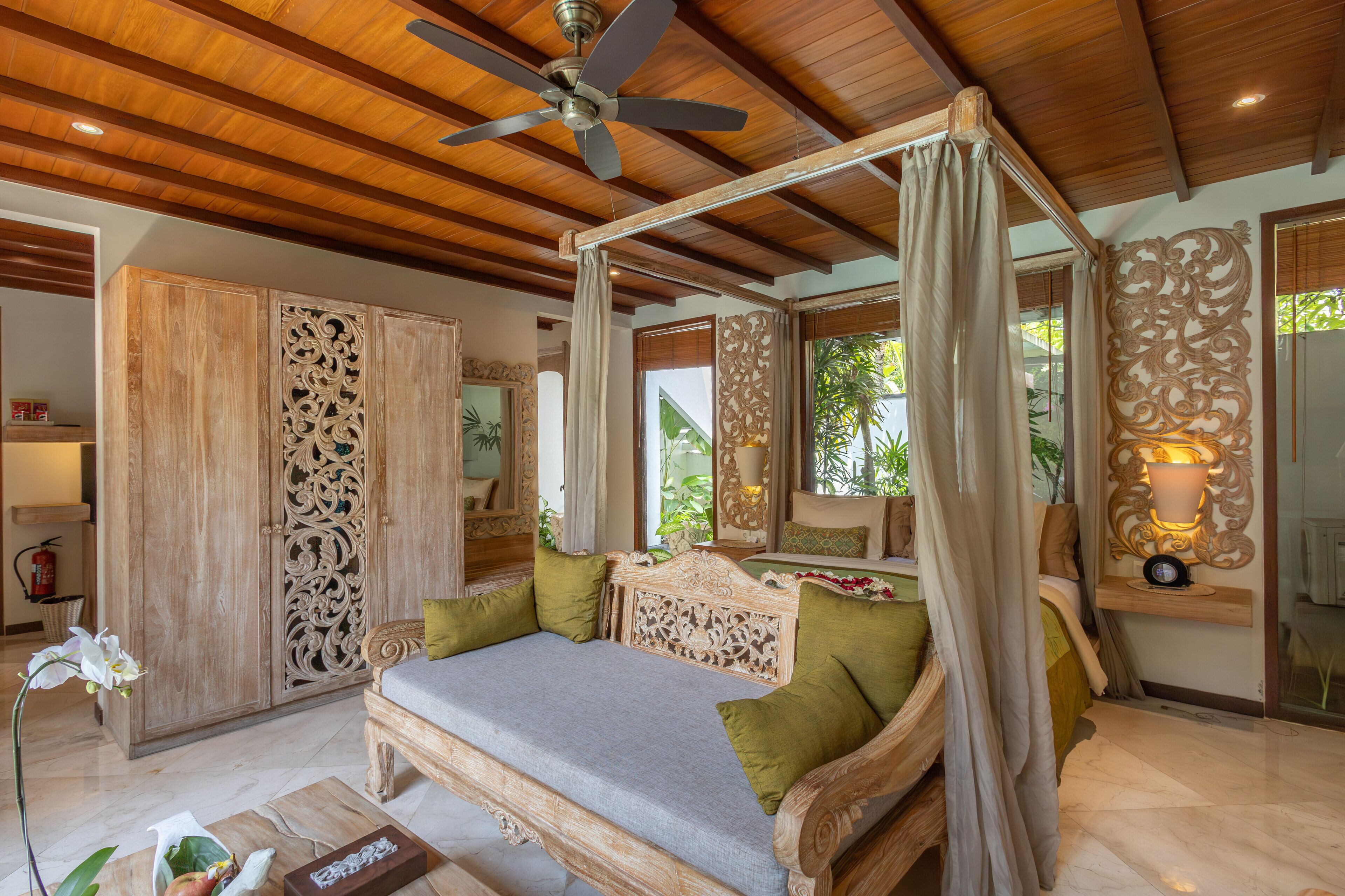 A four-poster canopy bed with green pillows, a wooden ceiling, and a ceiling fan.