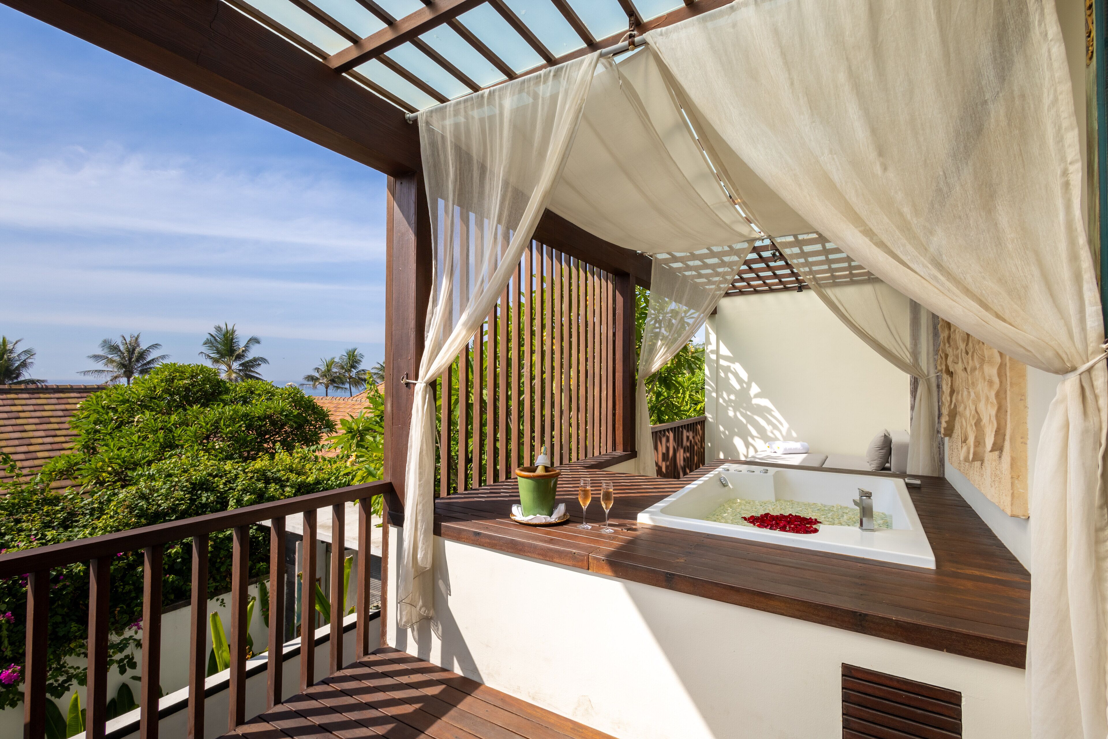 A balcony with a wooden floor, a white bathtub, and a green potted plant.