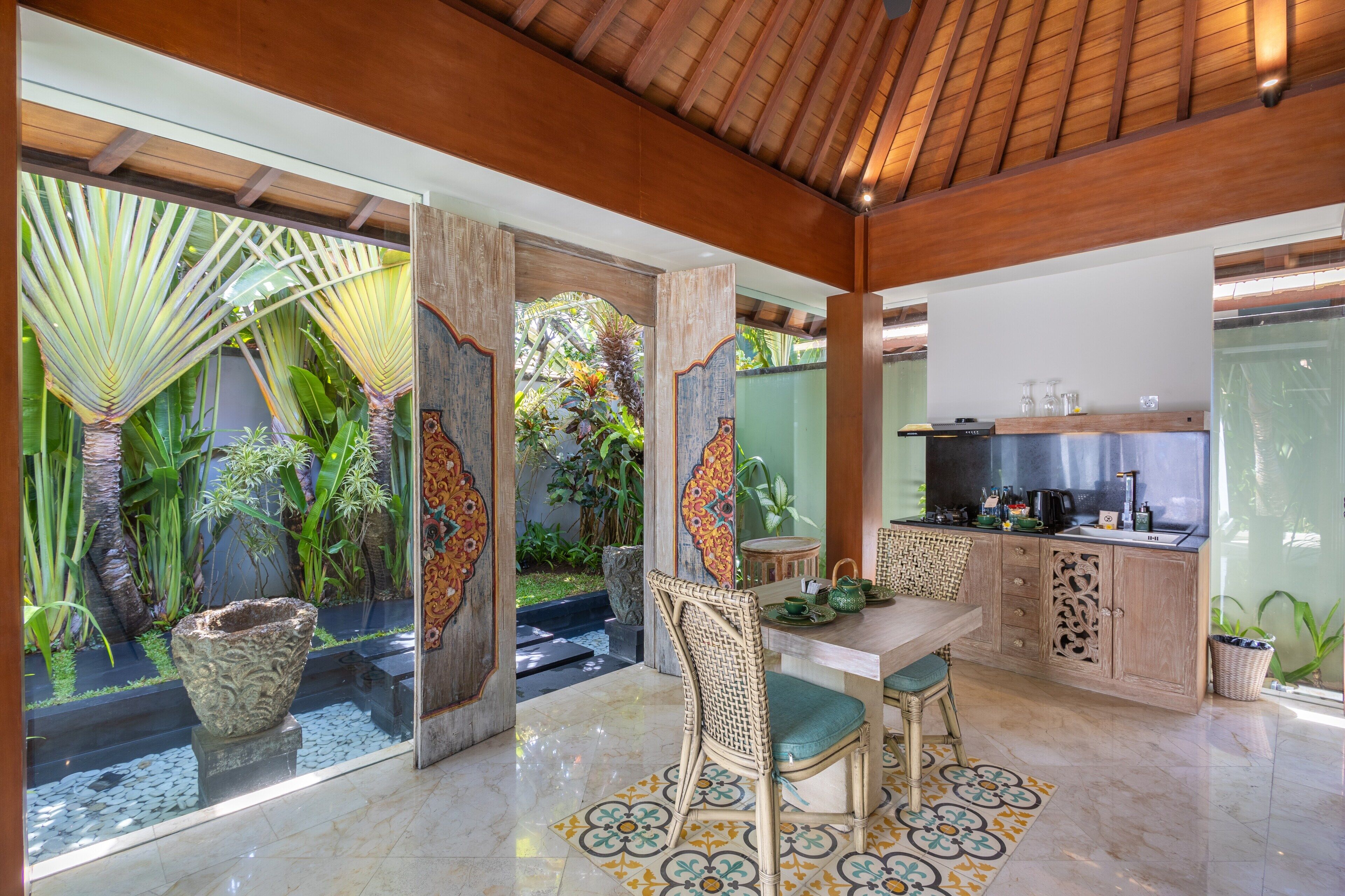 Una cocina moderna con comedor, techo de madera y vistas a un jardín tropical.