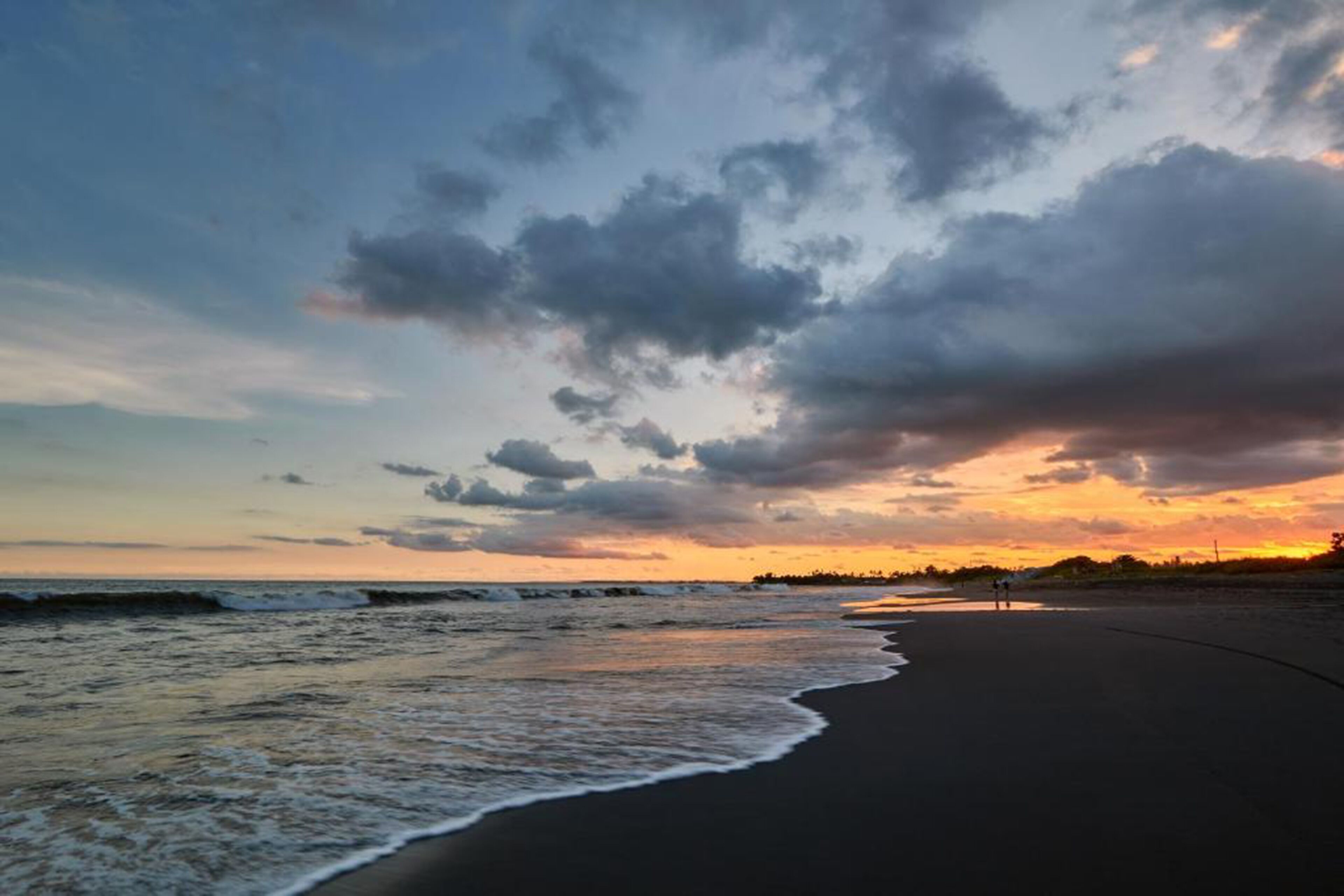 A beach with a curved shoreline, waves, and a sunset sky.