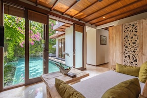 A bedroom with a large bed, a view of a swimming pool, and a wooden ceiling.