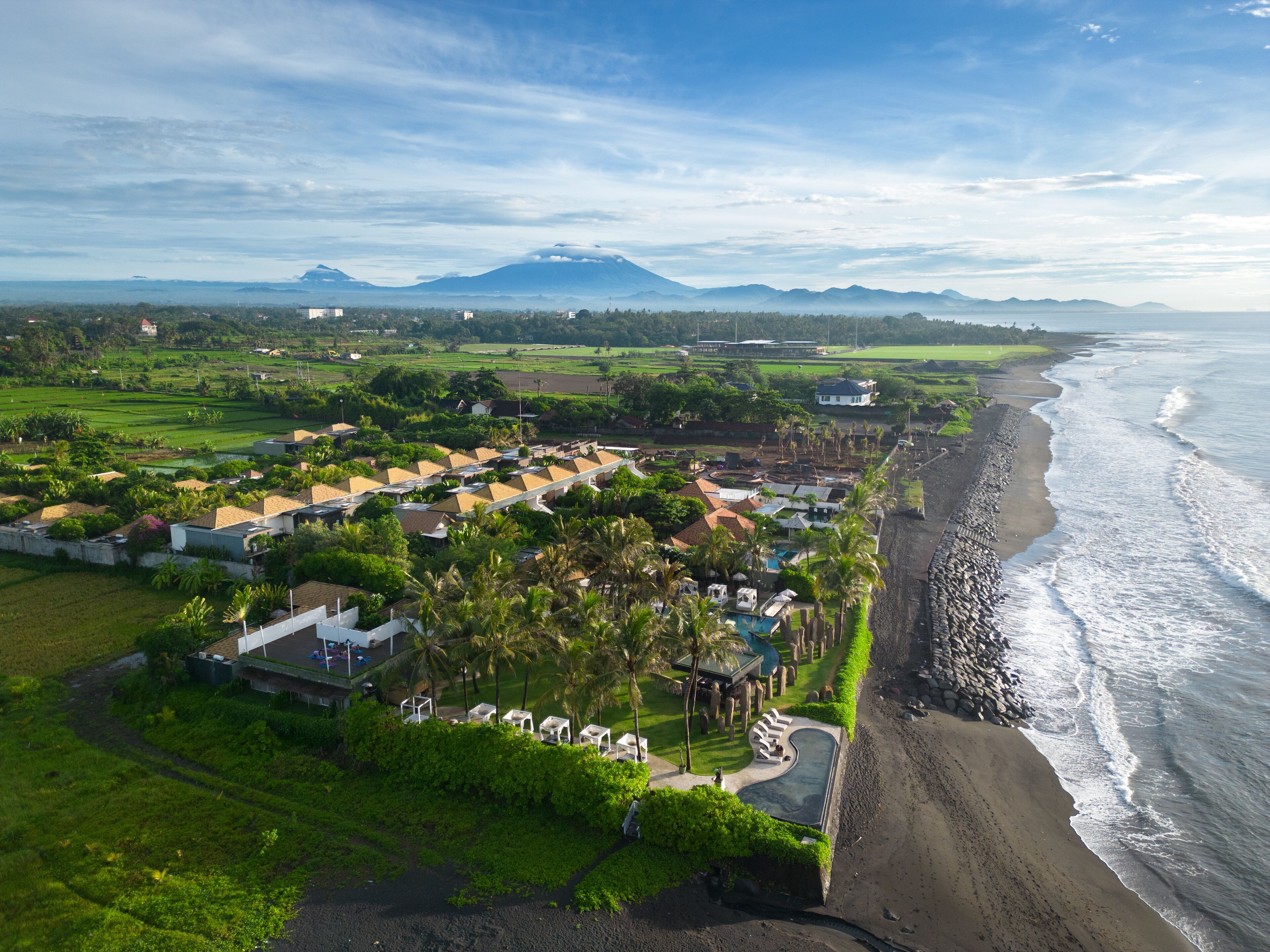 Un complejo turístico frente al mar con villas privadas, zona de piscina y vistas al océano y las montañas.