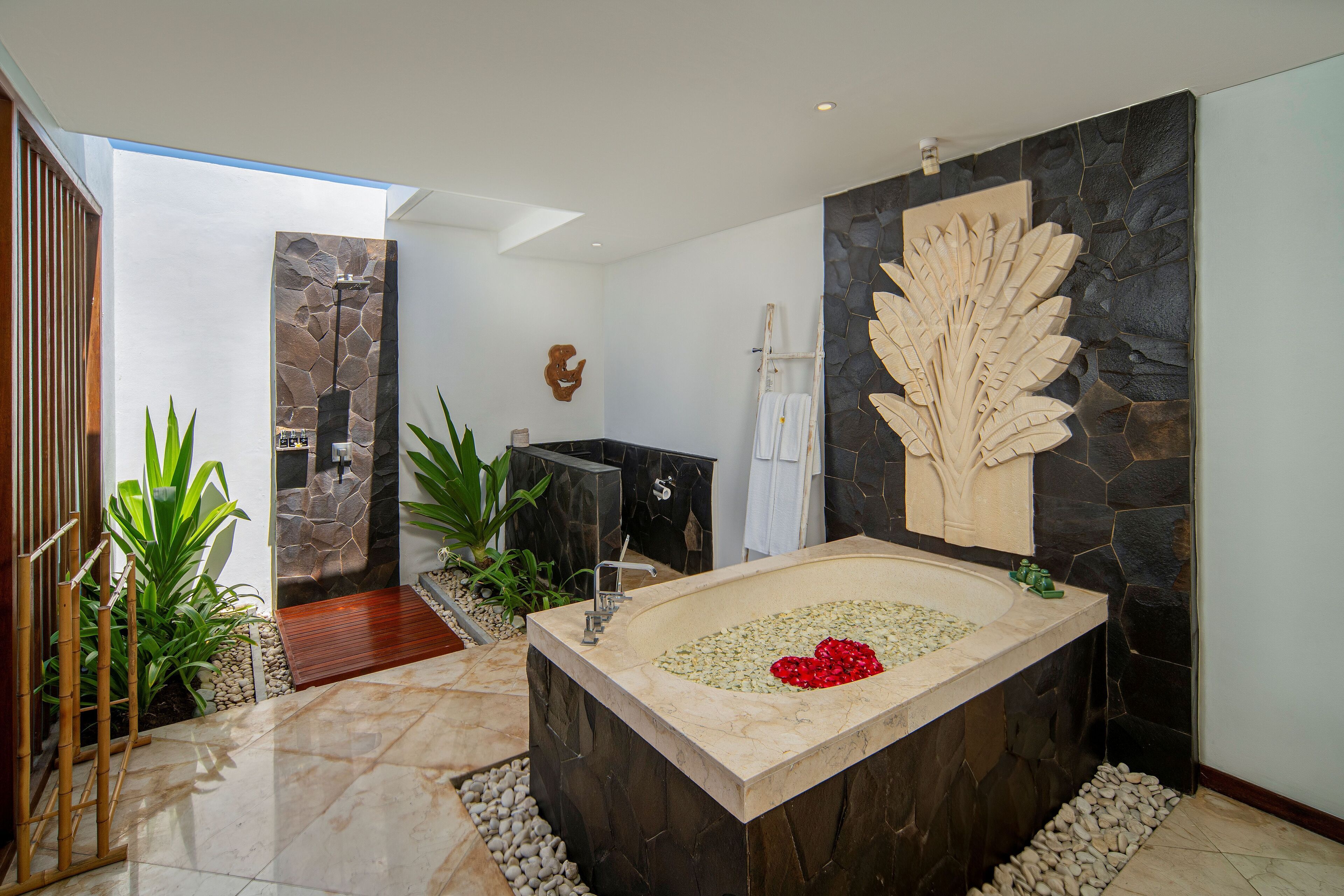 A modern bathroom with a large bathtub, stone walls, and a decorative leaf wall piece.