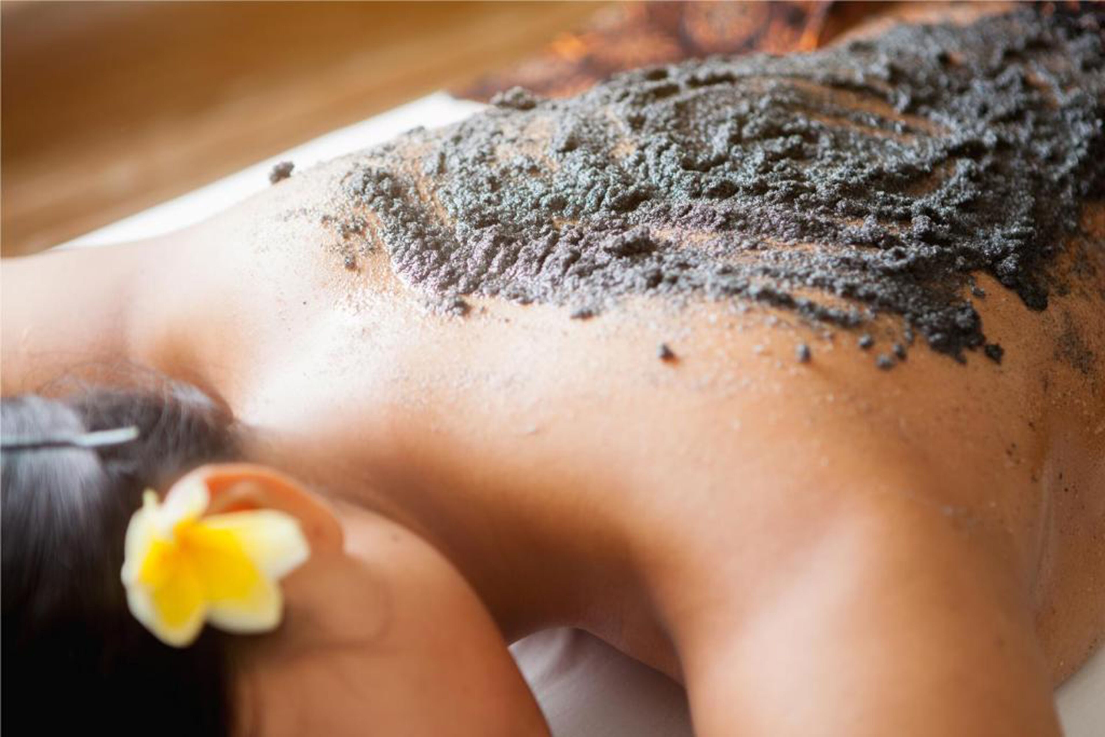 A person lying face down with a flower in their hair, suggesting a spa or relaxation setting.