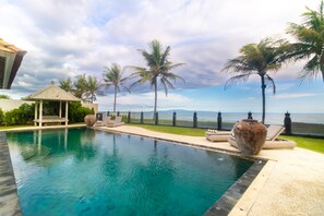 A pool with a view of the sea, surrounded by palm trees and lounge chairs. - The Royal Purnama Luxury Villas - Adults Only (Sukawati)