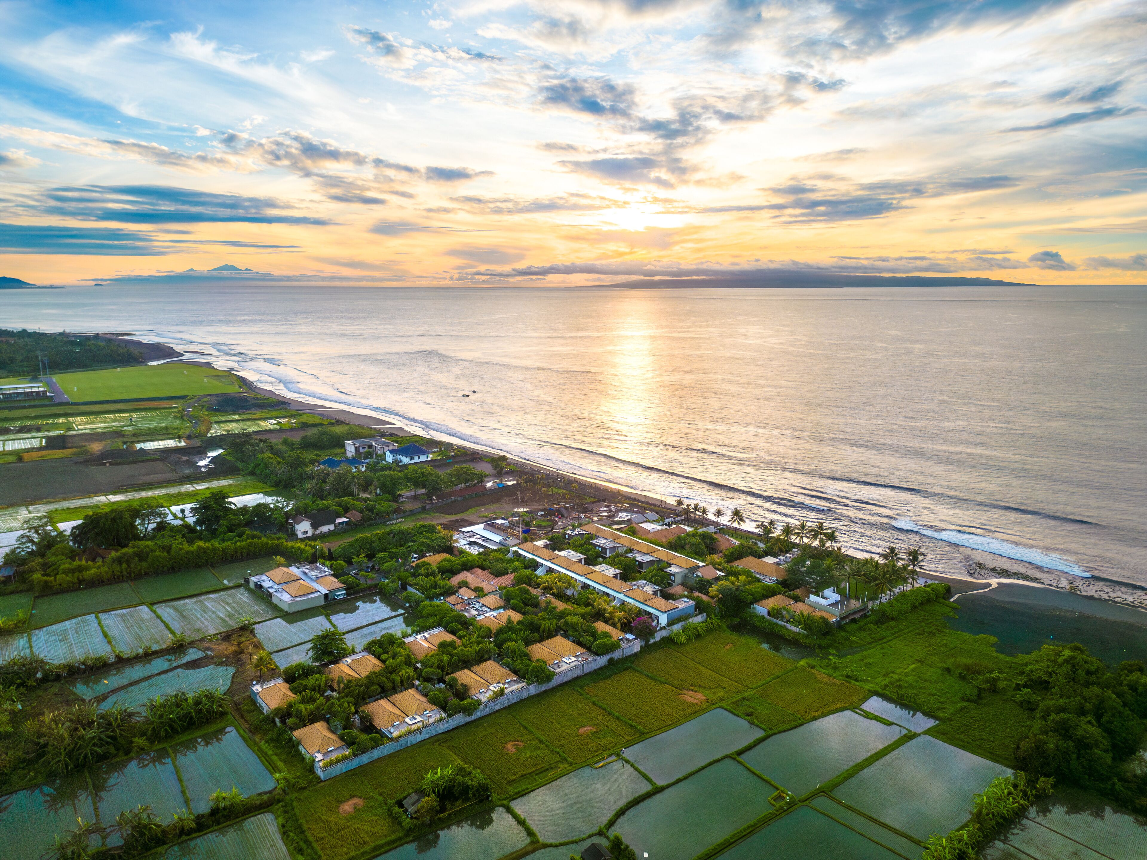 Vue aérienne d’un village côtier avec des champs en terrasses, des maisons et une plage.