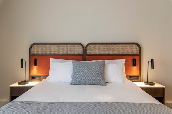 A neatly made bed with a patterned bedspread, two pillows, and two bedside lamps on wooden nightstands. - Kerkyra Blue Hotel & Spa by Louis Hotels (Corfu)