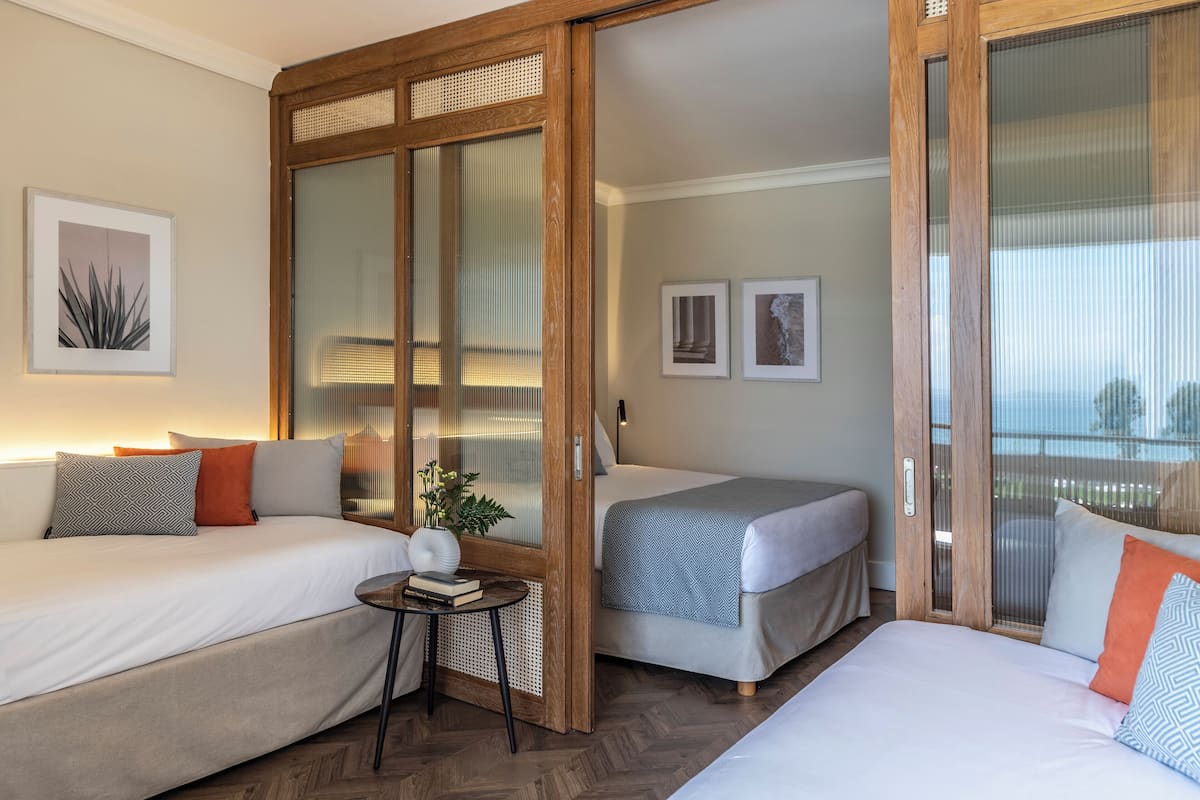 A hotel room with two beds, a small table, and a sliding door.