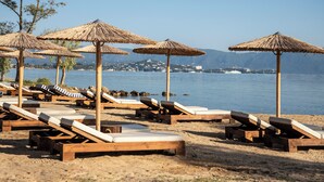 A beach with wooden lounge chairs and thatched umbrellas, overlooking a calm sea and distant hills. - Kerkyra Blue Hotel & Spa by Louis Hotels (Corfu)