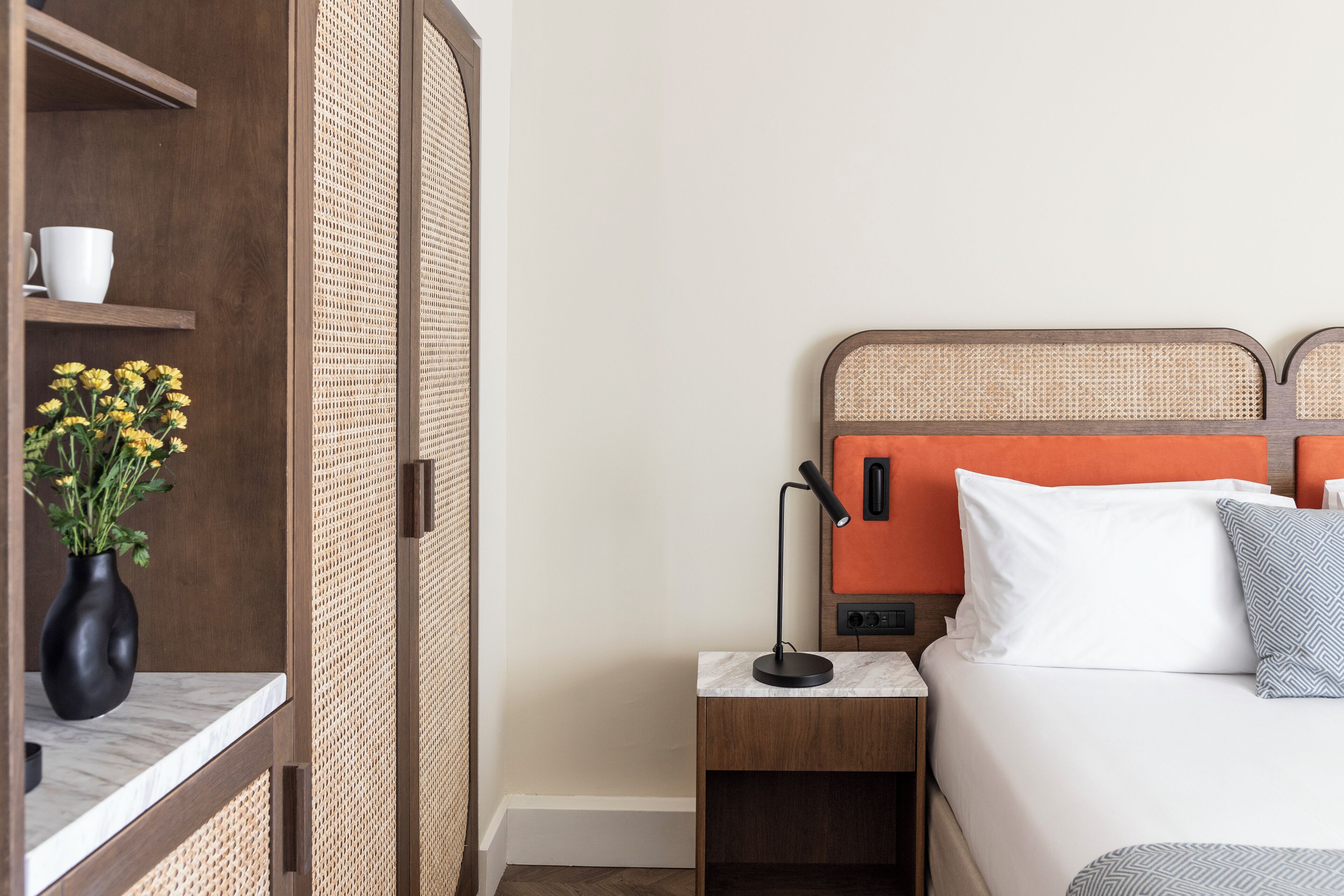 Camera d'albergo con un letto, un comodino, una lampada, un vaso con fiori e un armadio.