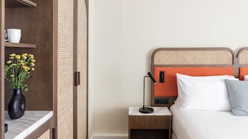 Camera d'albergo con un letto, un comodino, una lampada, un vaso con fiori e un armadio.