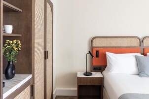 Camera d'albergo con un letto, un comodino, una lampada, un vaso con fiori e un armadio.