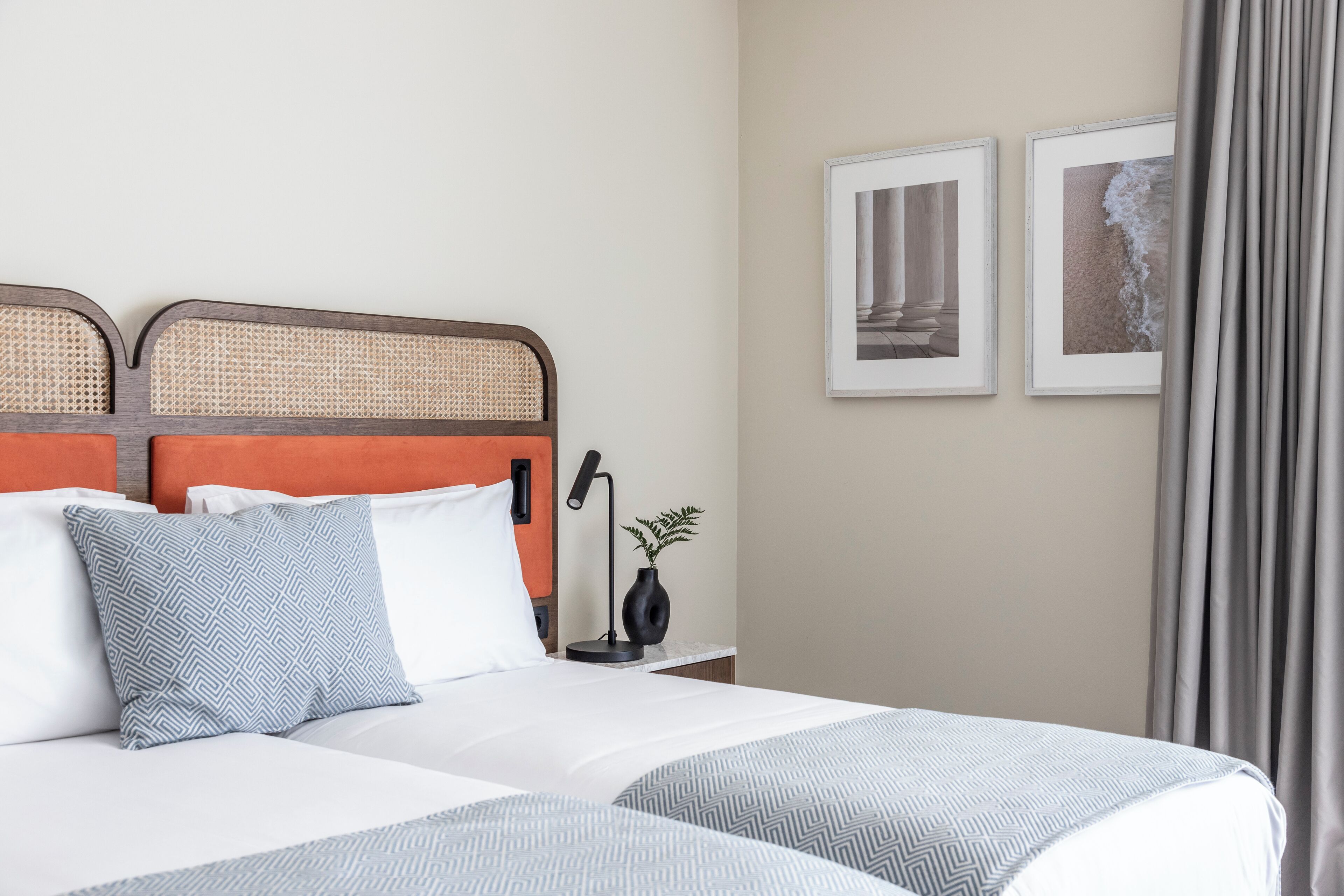 A hotel room with a bed, two pillows, a nightstand with a lamp, and framed pictures on the wall.