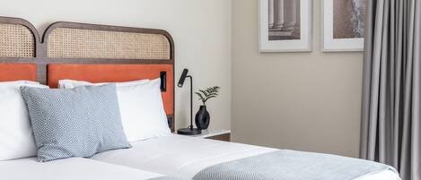 A hotel room with a bed, two pillows, a nightstand with a lamp, and framed pictures on the wall.