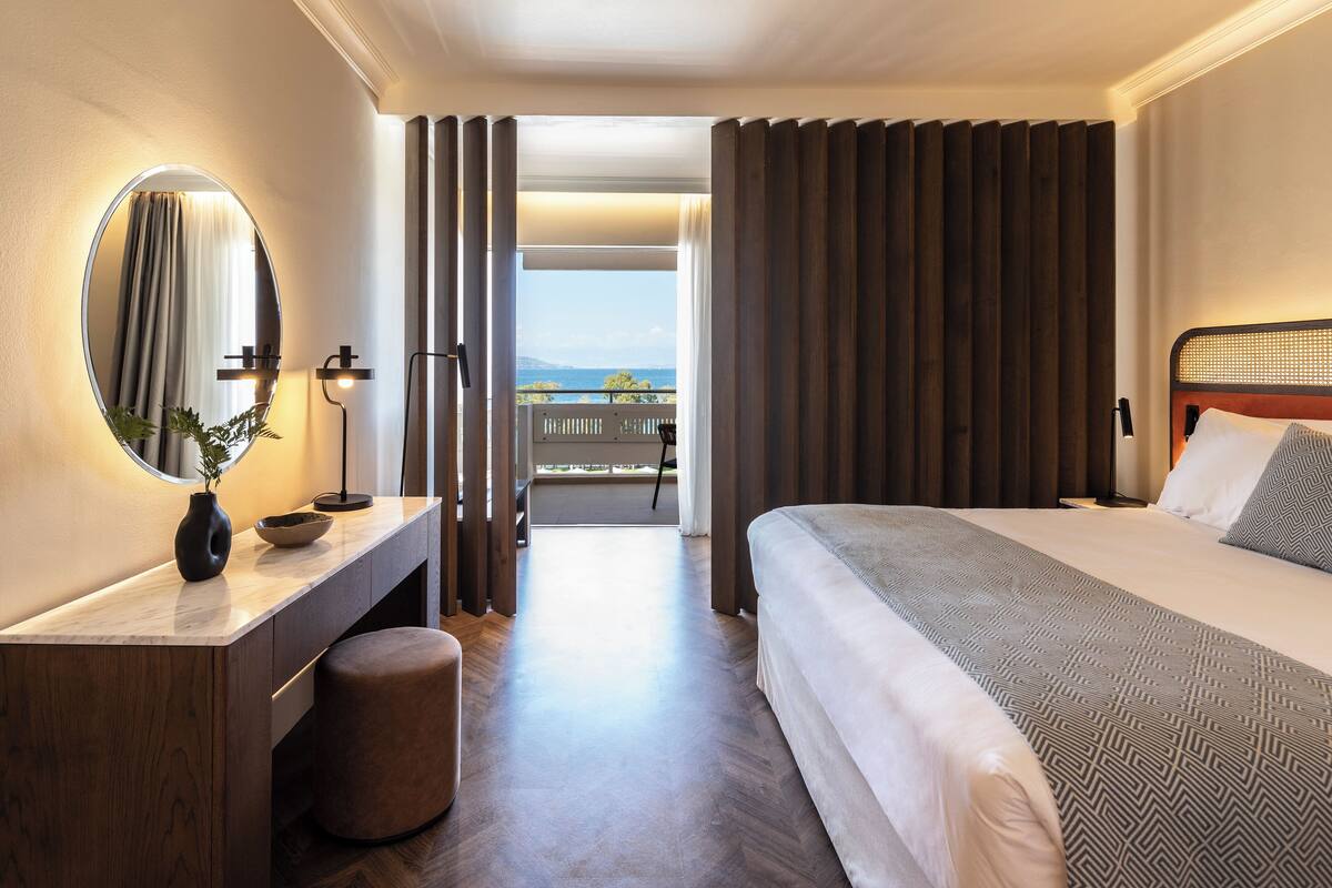 A hotel room with a bed, a bedside table with a vase, a mirror, and a view of the balcony.