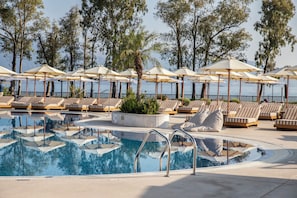 A pool area with lounge chairs and umbrellas, surrounded by trees and overlooking a body of water. - Kerkyra Blue Hotel & Spa by Louis Hotels (Corfu)