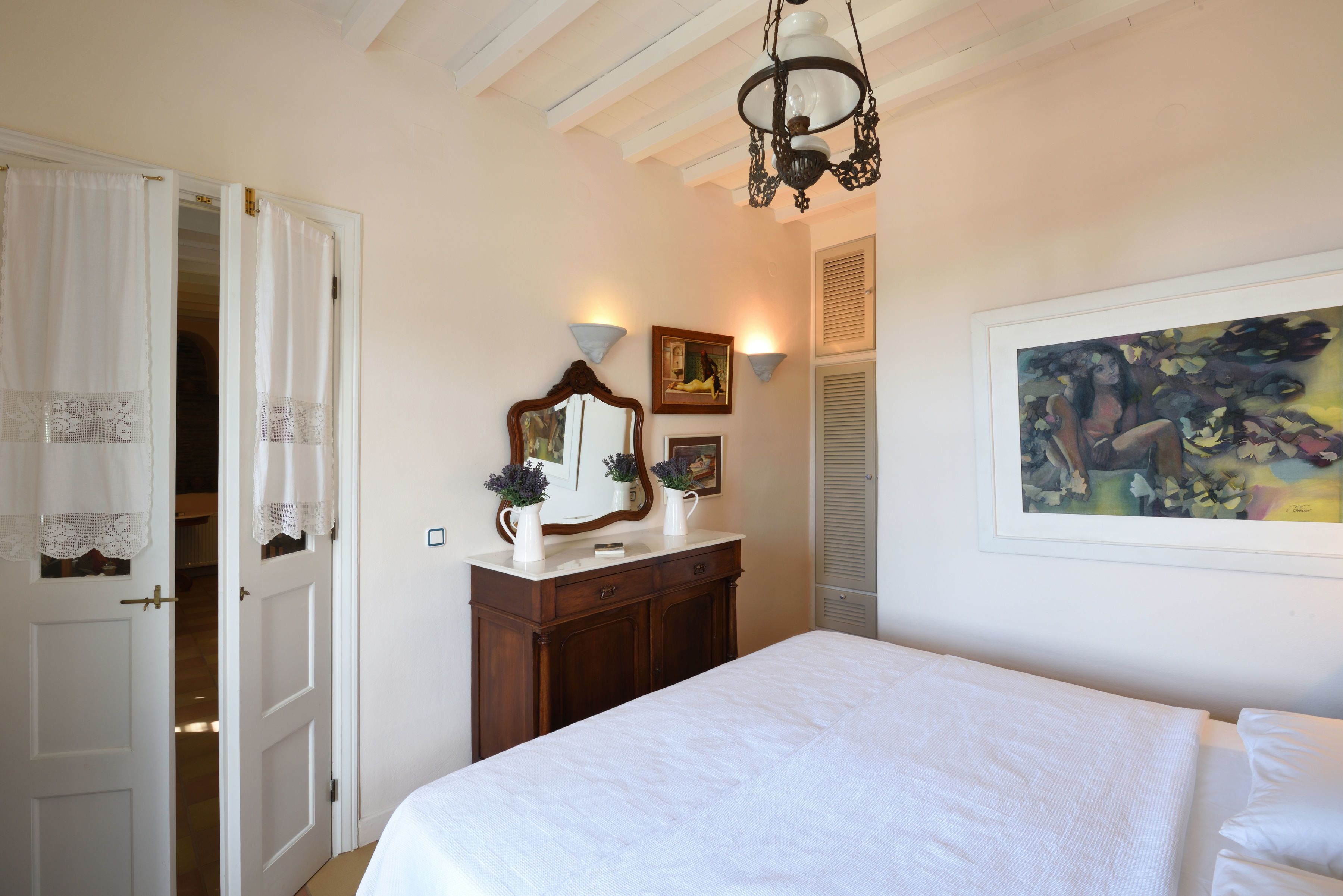 A bedroom with a bed, a dresser, a mirror, and a painting on the wall.
