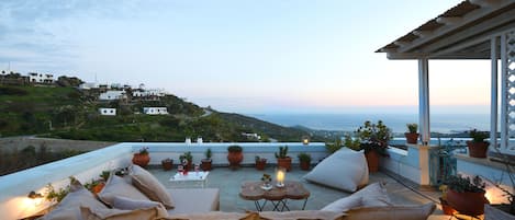 A rooftop terrace with a sofa, round tables, and potted plants.