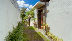 A narrow pathway flanked by white walls, leading to a building with a tiled entrance and a door with a colorful design. - The Canggu Boutique Villas (Tibubeneng)