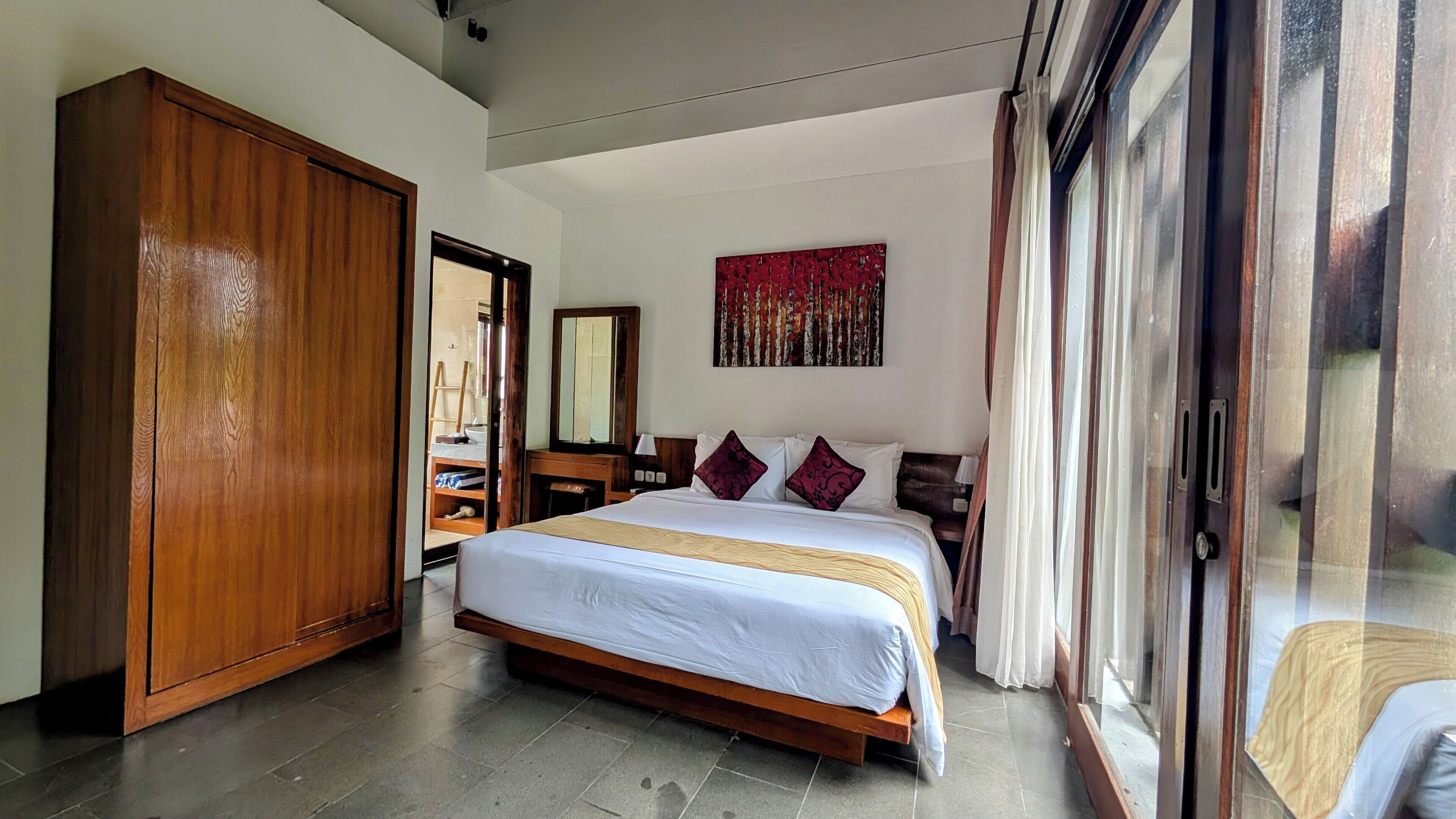 A bedroom with a large bed, wooden wardrobe, and a sliding glass door leading to a balcony.