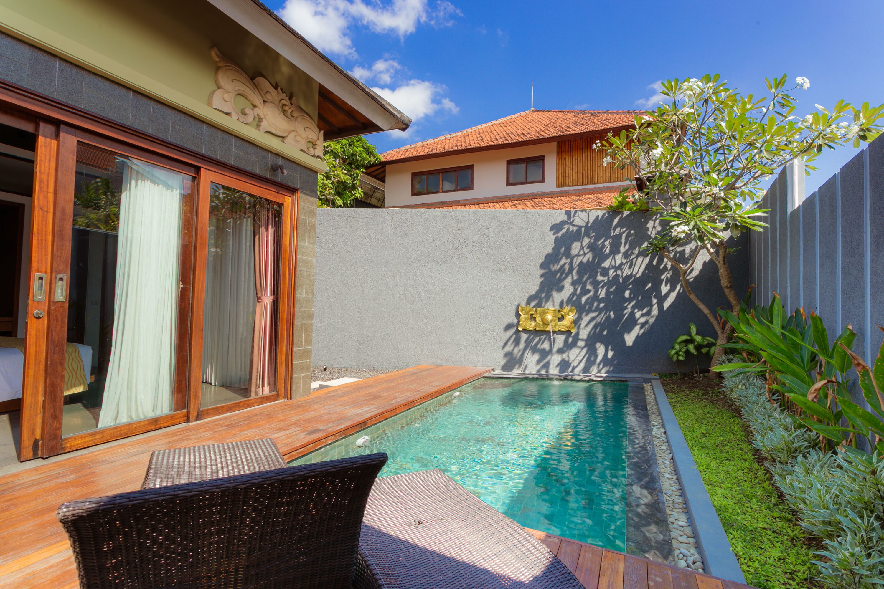 A swimming pool with a wooden deck and a wicker chair.