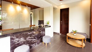 A modern reception area with a marble counter, two grey stools, a wooden round table with a plant, and a wooden door. - The Canggu Boutique Villas (Tibubeneng)