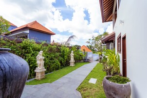 A pathway leading to a house with a red-tiled roof, surrounded by greenery and statues.