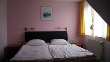 Ein Einzelbett in einem Zimmer mit rosafarbenen Wänden, einem gerahmten Bild an der Wand und einem Fenster mit Vorhängen.