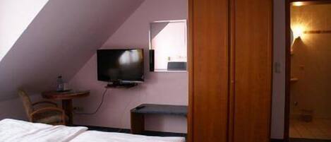 Un dormitorio con cama, televisor, escritorio y armario.