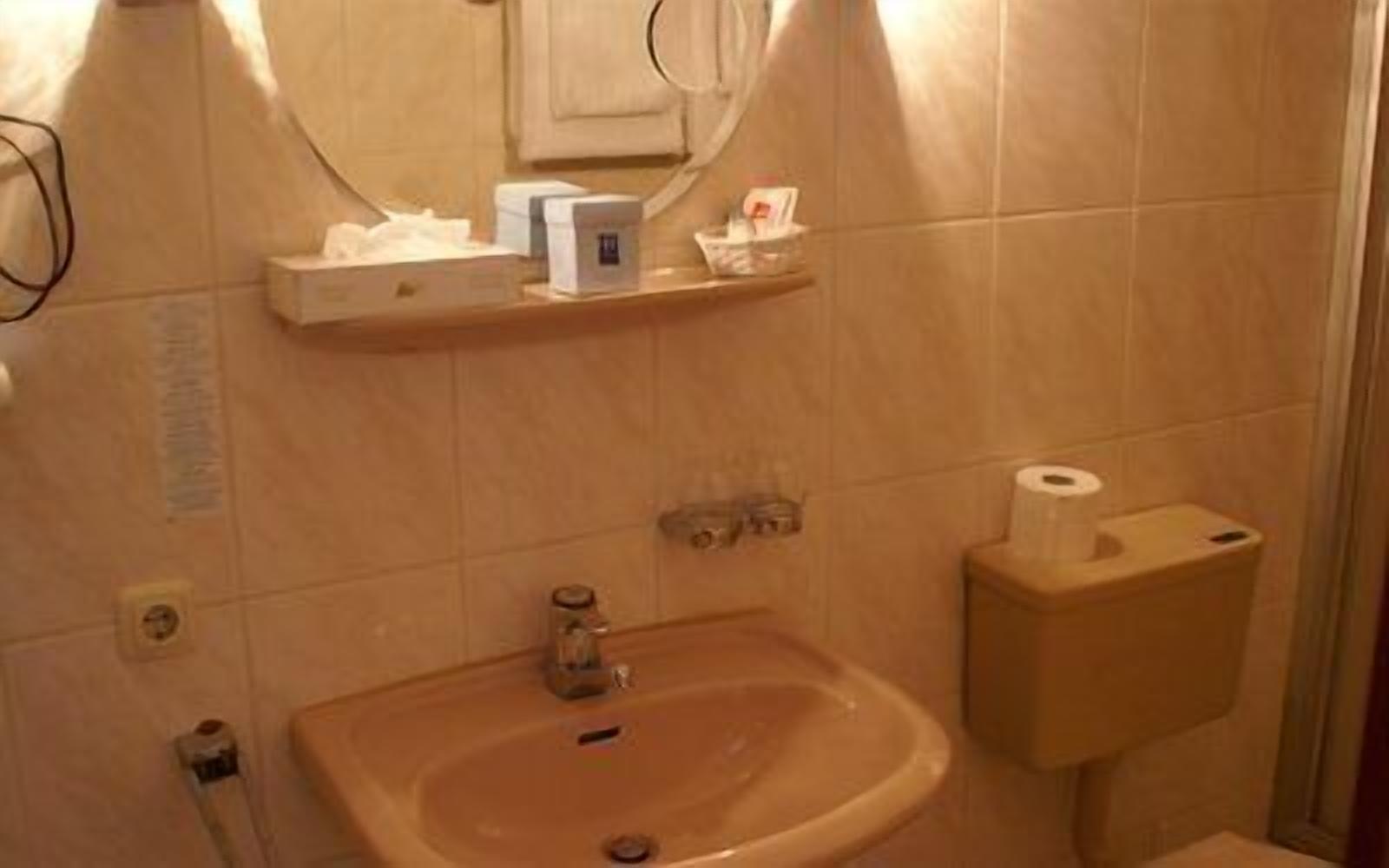 A bathroom with a sink, mirror, and toilet. There are toiletries on a shelf above the sink.