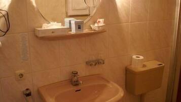 A bathroom with a sink, mirror, and toilet. There are toiletries on a shelf above the sink.