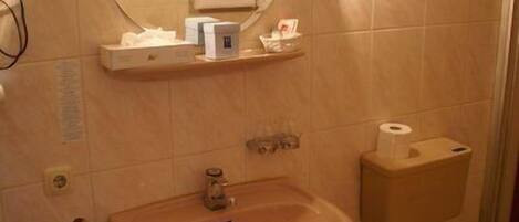 Un baño con lavamanos, espejo e inodoro. Hay artículos de aseo en un estante sobre el lavamanos.