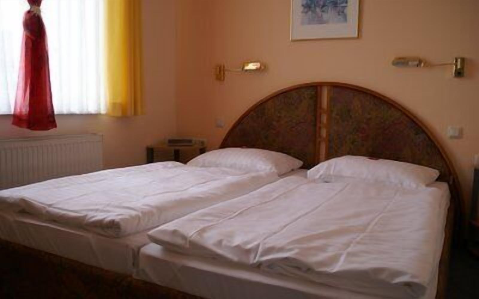 Ein Doppelbett mit weißen Laken in einem Zimmer mit Holz-Kopfteil, einem Heizkörper und einem gerahmten Bild an der Wand.