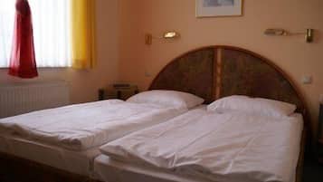 Ein Doppelbett mit weißen Laken in einem Zimmer mit Holz-Kopfteil, einem Heizkörper und einem gerahmten Bild an der Wand.