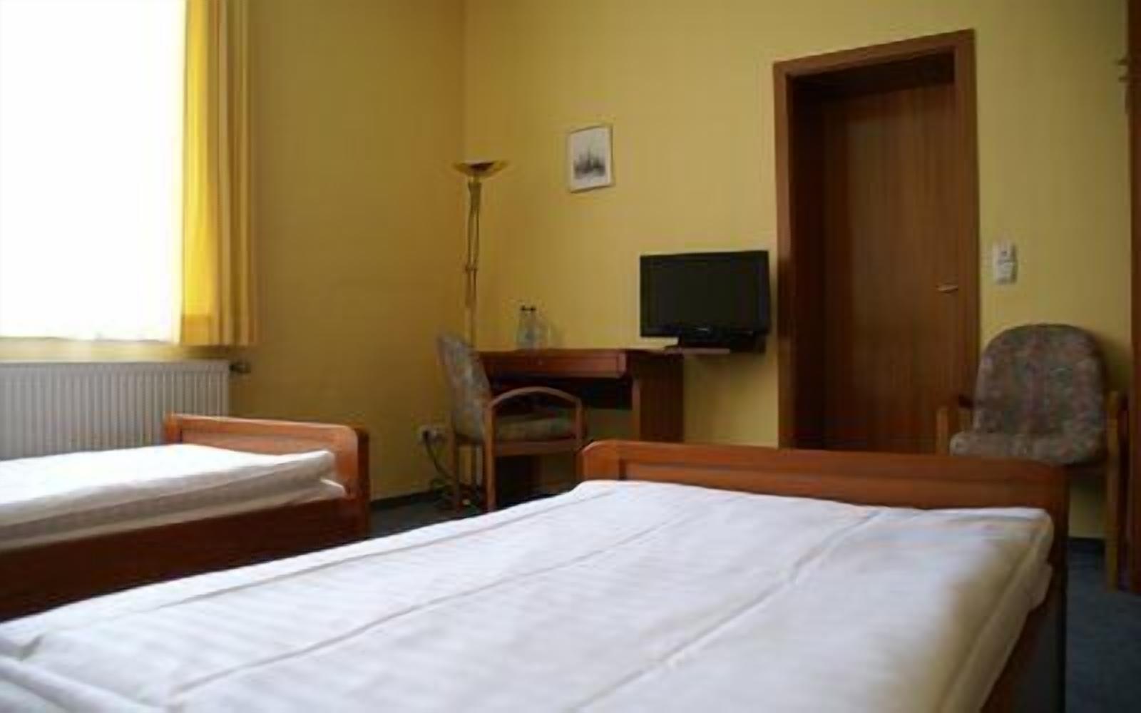 A hotel room with two single beds, a desk with a chair, a television, and a door.