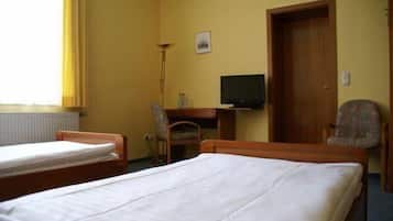 A hotel room with two single beds, a desk with a chair, a television, and a door.