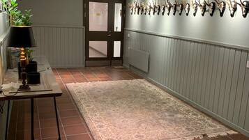 A hallway with a patterned rug, a table with a lamp, and a wall with mounted animal heads.