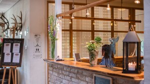 Un espace d’accueil avec un comptoir en briques, des poutres en bois, des luminaires suspendus et une plante.