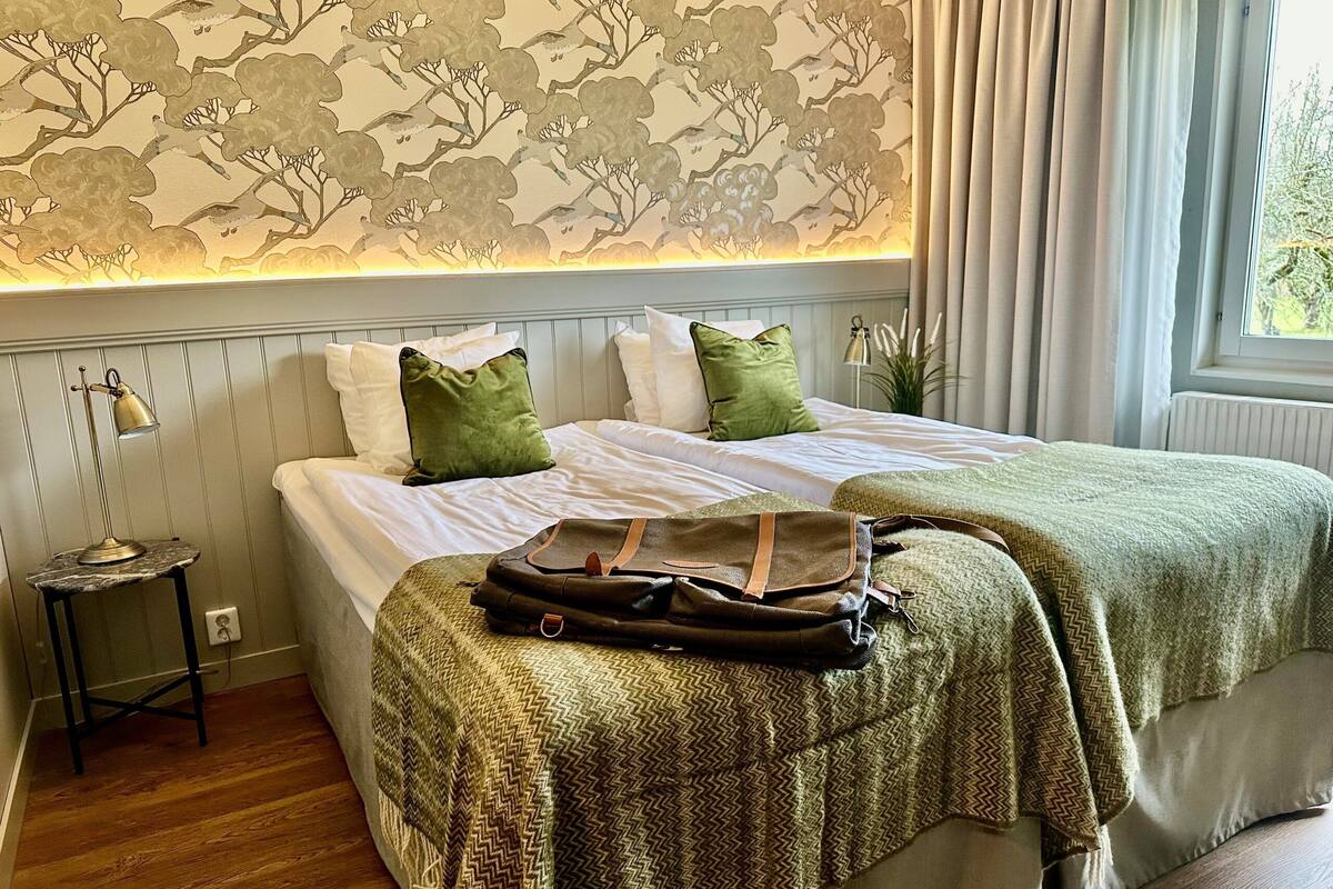 Un lit bien fait, avec deux oreillers, un plaid vert et un sac marron posé sur le lit.