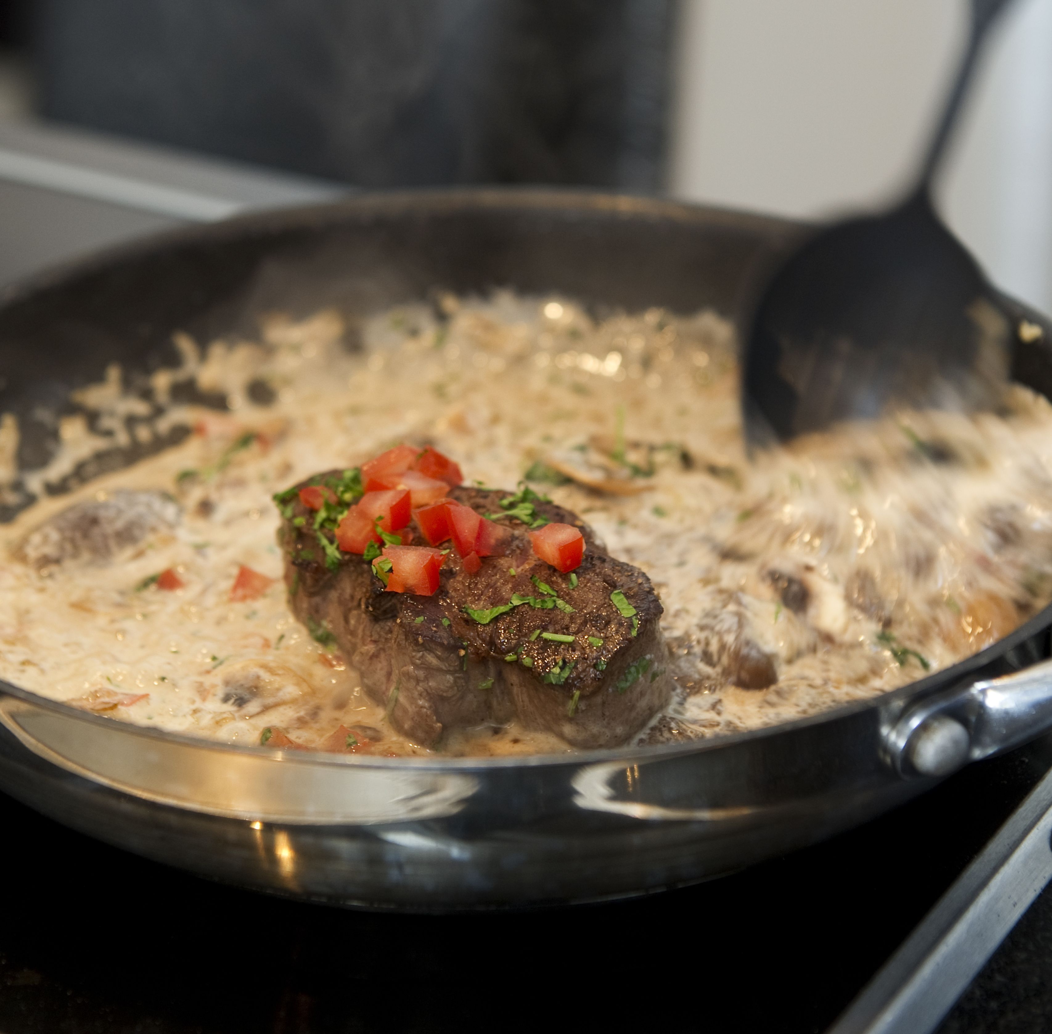 Un bistec en la sartén con salsa cremosa, decorado con tomates en cubitos y hierbas.