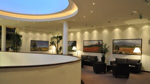 A reception area with a curved desk, multiple seating options, and framed landscape paintings on the walls. - Casino & Hotel ADMIRAL Kozina (Hrpelje-Kozina)