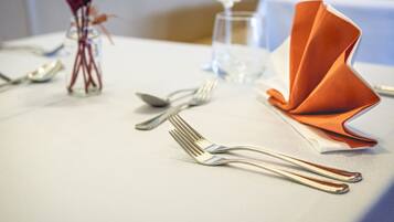 A table set with silverware, a folded orange napkin, and a clear glass.