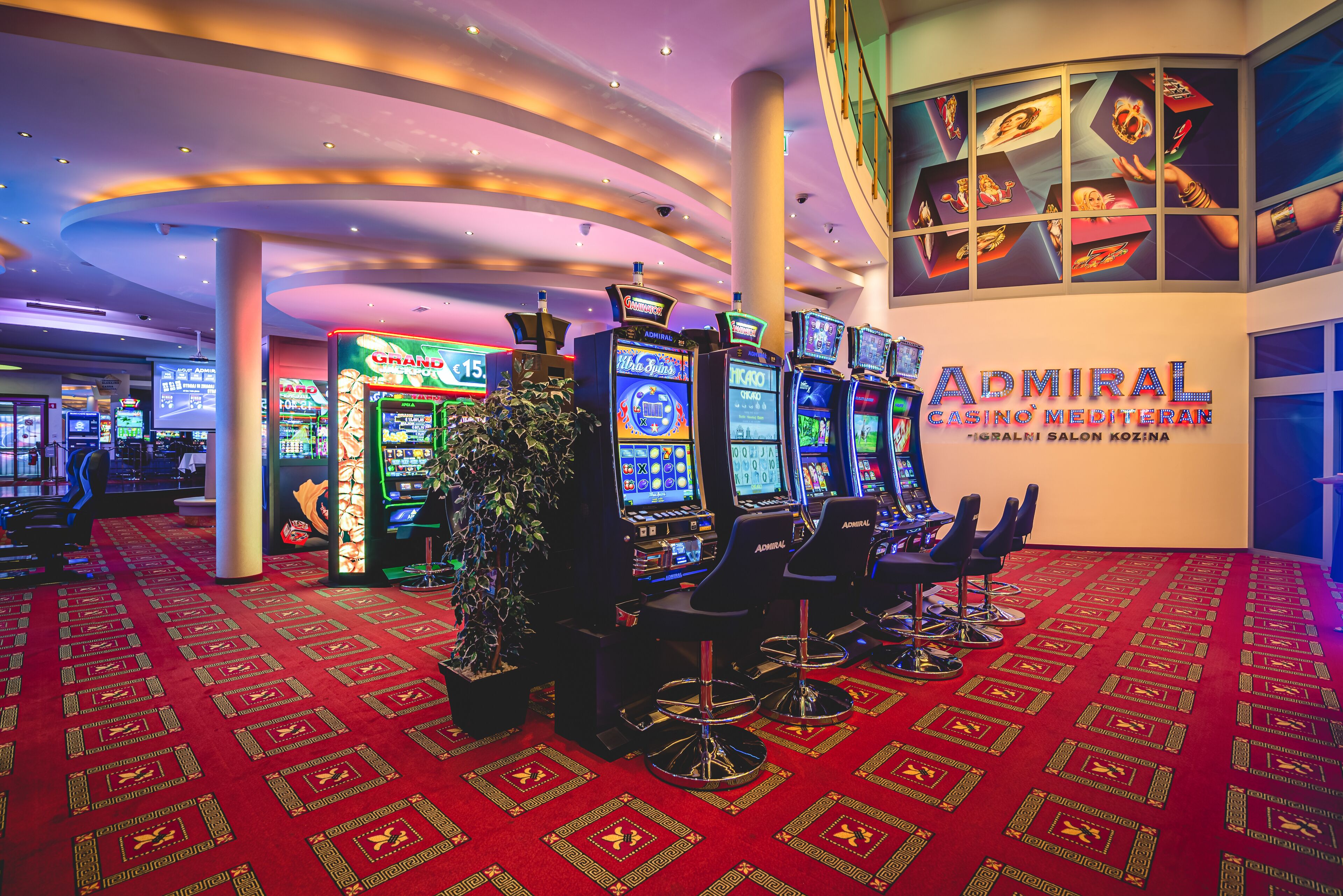 Ein Kasinobereich mit Spielautomaten, Barhocker und einem Schild für 'Admiral Casino Mediterranean'.