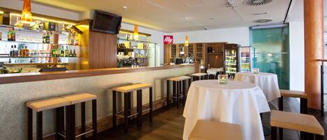 A bar area with stools, tables, and a television screen.