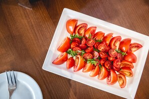 A white rectangular plate with sliced tomatoes and greens on a wooden table.