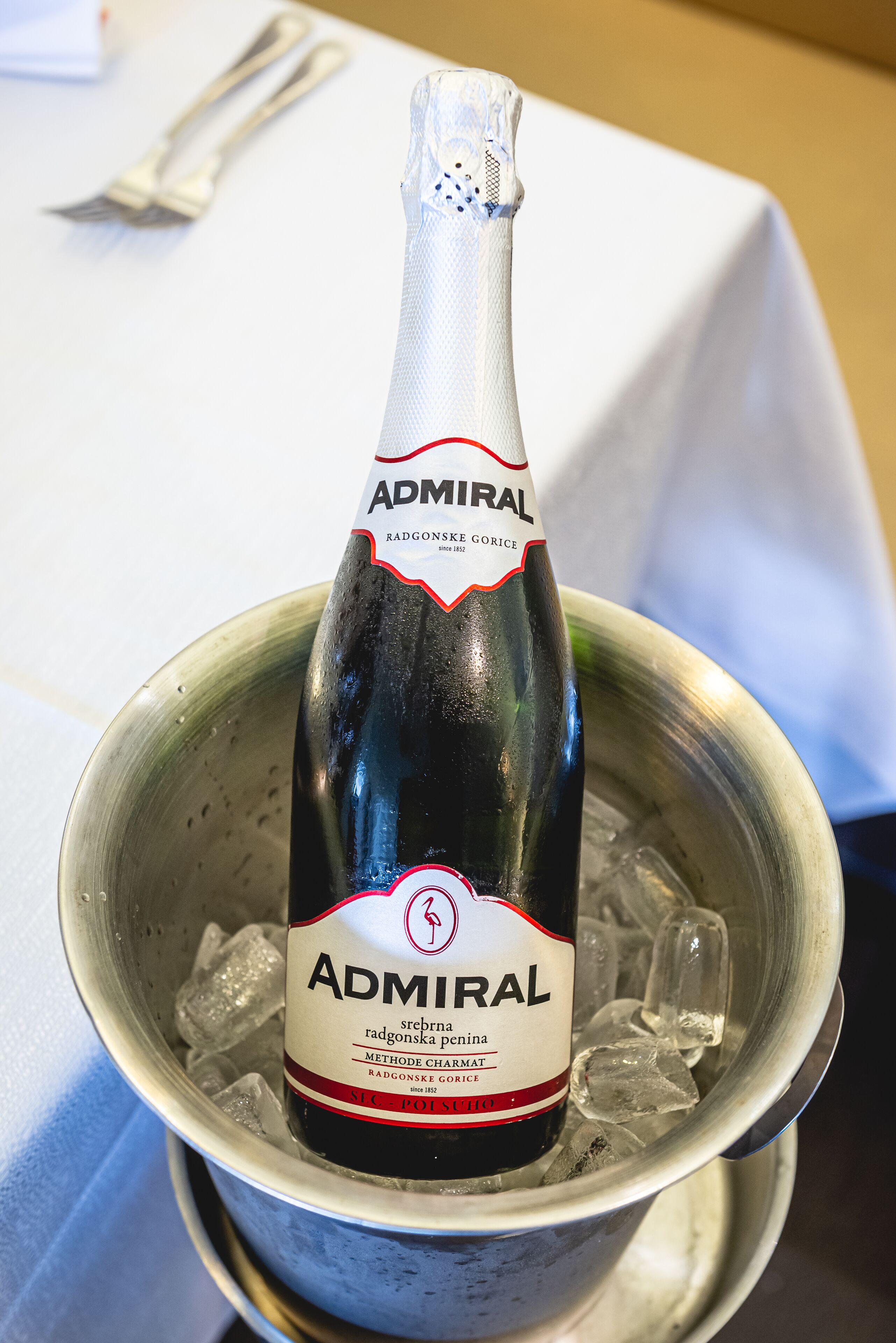 Una botella de champán Admiral Radgonske Gorice en un balde de metal con cubitos de hielo.