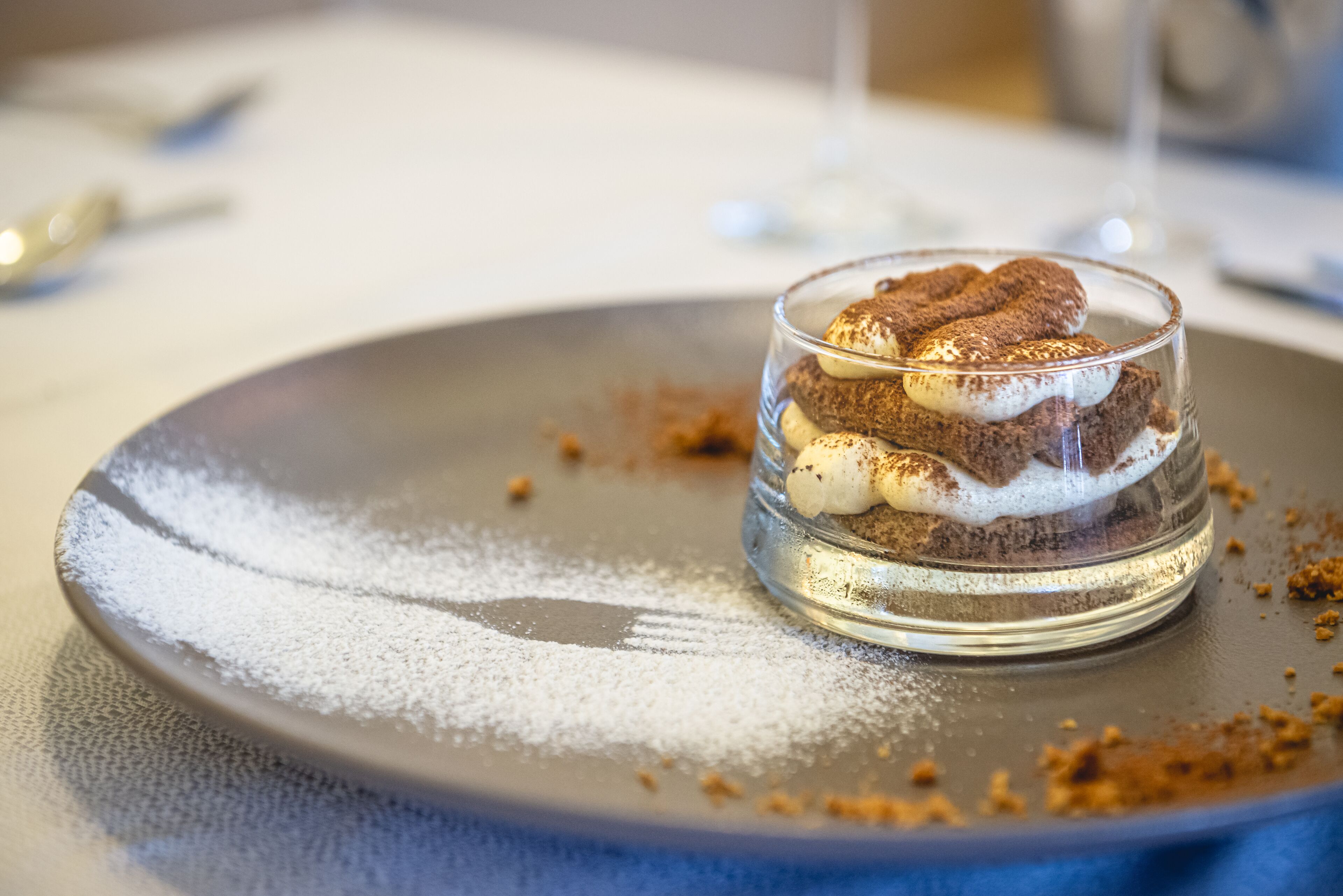 A dessert in a glass on a plate with powdered sugar on the table.